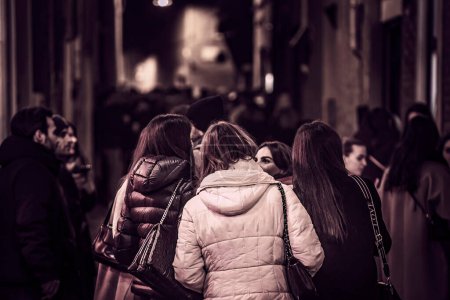 Foto de Ferrara, Italy 5 February 2023: A group of young girls navigating through a crowded city center at night, surrounded by historic buildings - Imagen libre de derechos