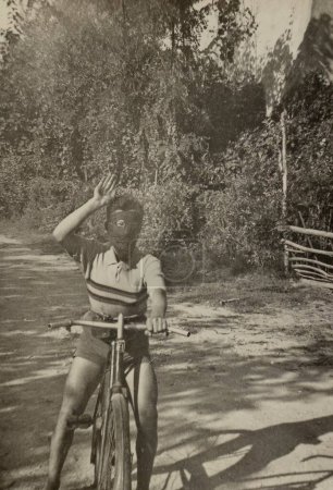 Foto de Roma, Italia mayo 1951: Foto vintage de un joven alborotador italiano con un pañuelo cubriéndose la cara, montando en bicicleta en la década de 1950. - Imagen libre de derechos