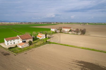 This aerial view showcases a farm situated in the middle of a vast field, surrounded by crops and agricultural infrastructure. The farm appears to be actively cultivated, with barns, silos, and equipment visible from above.