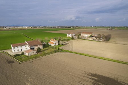 This aerial view shows a farm with a house located in the center. The surrounding fields are neatly organized with crops and livestock visible.