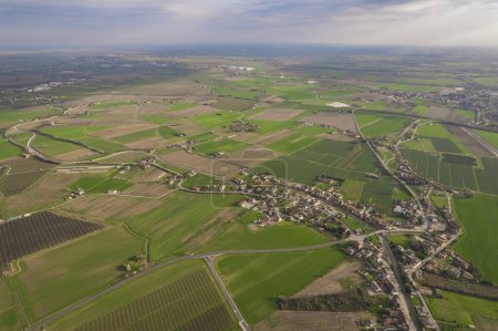 This aerial view captures a vast rural area in the Pianura Padana region, characterized by endless green fields and farmland stretching as far as the eye can see. The landscape is dotted with clusters of trees and farm buildings, showcasing the agric