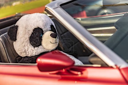 A cuddly panda plush toy sits in the seat of a classic American vintage car, evoking nostalgia.