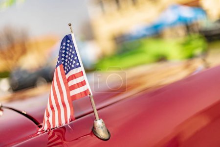 Vicenza, Italy 19 March 2024: An American flag draped over the hood of a vibrant red car.