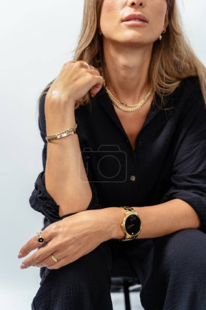 Foto de Retrato vertical de mujer madura atractiva en modelo de desgaste negro que muestra pulseras doradas, anillos, cadenas sobre fondo blanco. - Imagen libre de derechos