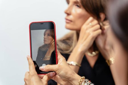 Foto de Retrato de una atractiva blogger madura en modelo de desgaste negro mostrando pulseras doradas, anillos, cadenas sobre fondo blanco. - Imagen libre de derechos