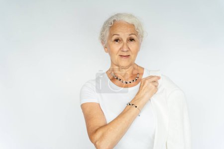 Photo for Happy senior grey hair woman portrait wearing white clothes showing jewellery bijouterie on white background. - Royalty Free Image