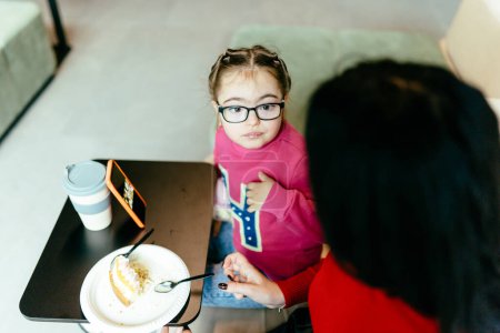 Téléchargez les photos : Petite fille mignonne dans les lunettes en utilisant smartphone intérieur dans le hall ou café. Concept enfants et gadgets. - en image libre de droit