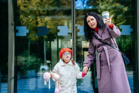 Photo for Cute lovely positive brunette mother talking with her happy disabilities daughter outdoor. Woman and child enjoy walk autumn sunny day outside the business center. - Royalty Free Image
