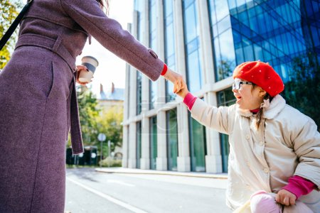 Photo for Cute little girl in red wear beret and coat in eyeglasses, whirling frolicking and playing with her unrecognizable mother at autumn sunny day city street outdoor. - Royalty Free Image