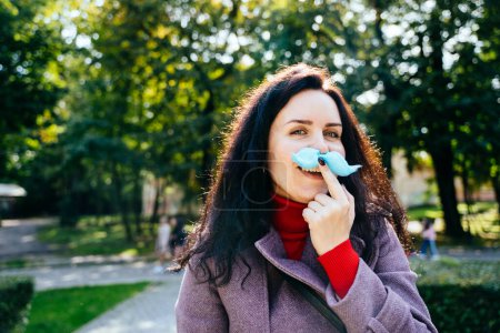 Téléchargez les photos : Portrait d'une mère d'âge moyen faisant un geste de moustache de barbe à papa bleue à la caméra dans un parc d'attractions à l'automne. - en image libre de droit
