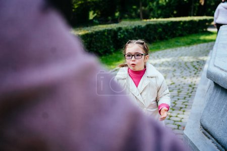 Photo for Portrait sad down syndrome girl in eyeglasses standing in front of her mother with a sad face, crying talking. - Royalty Free Image