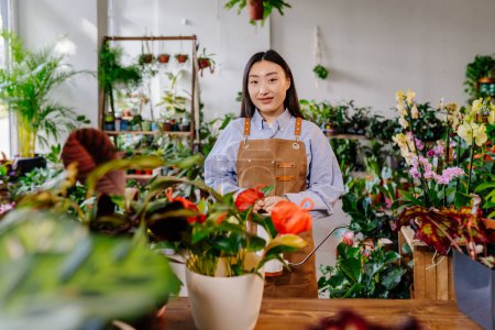 Foto de Inicie el concepto de pequeña empresa. Retrato de una joven propietaria coreana de pie usando delantal detrás del mostrador en el interior de la tienda de plantas de flores. - Imagen libre de derechos