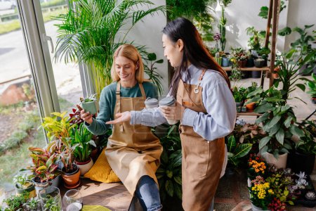 Photo for Waist up shot of two smiling gardeners looking at pot with small plant indoors while working together with lush green plants. - Royalty Free Image