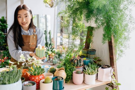 Photo for Small business, home decor concept. Professional young Asian female floral store owner arranges flower pots, takes stock daily routine of running a small business. Small business concept. - Royalty Free Image