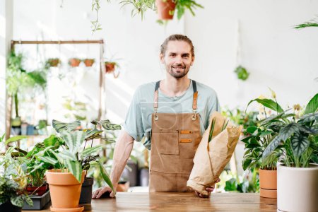 Foto de Retrato de vendedor caucásico guapo positivo, empleado vendiendo plantas en maceta en una tienda de flores. Pequeños empresarios. - Imagen libre de derechos