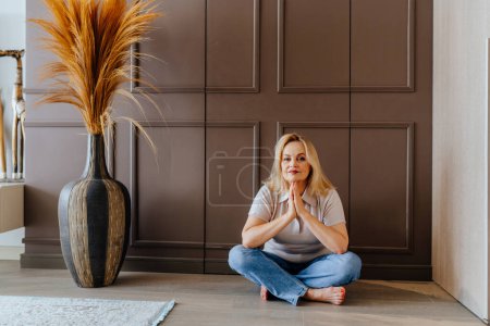 Téléchargez les photos : Portrait de femme amicale positive confiante réfléchie assise sur le sol à l'intérieur de la maison confortable. - en image libre de droit