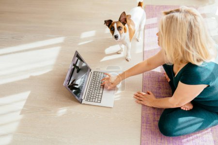Téléchargez les photos : Fit sportif en bonne santé mature corps d'âge moyen femme positive s'asseoir sur le tapis faire des exercices de respiration, regarder des cours de yoga en ligne sur ordinateur portable. - en image libre de droit