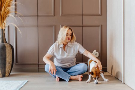 Photo for Happy middle aged woman sitting on the floor petting hugging her beloved pet dog Jack Russell at home living room. Home activity, leisure time concept. - Royalty Free Image