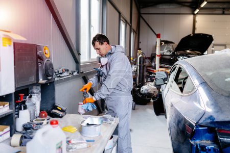 Männlicher Maler Techniker Anwendung roter Farbe in die Spritzpistole im Auto-Service-Center Autoreparatur Karosserielack-Werkstatt.