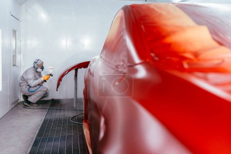Photo for Professional male car mechanic working with spray gun painting part of auto body in automotive paint service shop. Automobile painter painting car in chamber. - Royalty Free Image