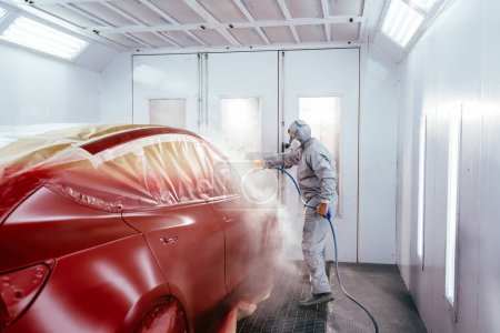 Téléchargez les photos : Réparateur professionnel peinture de voiture dans une cabine de pulvérisation à un service de voiture professionnelle. - en image libre de droit