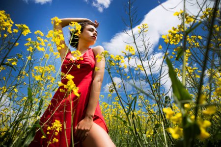 Foto de Young girl dressed in red dress in a field of yellow flowers in summer season - Imagen libre de derechos
