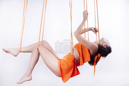 Téléchargez les photos : Photo documentation of a beautiful hanging girl in an orange dress hanging on ropes - en image libre de droit