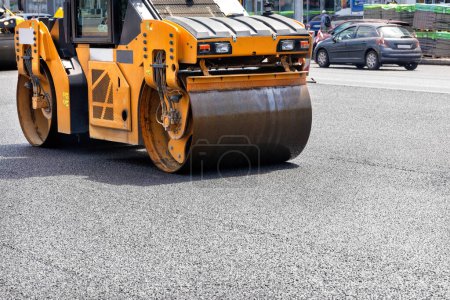 Photo for A vibrating roller rams and compacts fresh asphalt on a city street on a summer day among the roadway. Close-up. Copy space. - Royalty Free Image