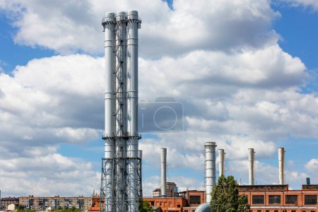 Photo for The tall triple stacks of the city's thermal power plant rise above city houses against a blue cloudy sky. - Royalty Free Image