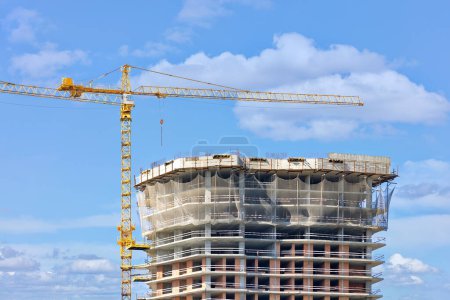 Photo for Tower crane on the background of the construction of a multi-storey high-rise residential building against a blue cloudy sky. Copy space. - Royalty Free Image