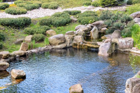 Photo for The stream flows into a garden pond bordered by stone boulders around the shoreline. - Royalty Free Image