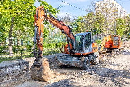 Photo for Large wheeled and crawler excavators are parked in a trench dug in the middle of a city street road on a bright sunny spring day. - Royalty Free Image