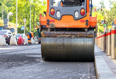 Photo for Road vibratory roller compacts fresh asphalt along the edge of the sidewalk on a city street road on a sunny day with high precision. - Royalty Free Image