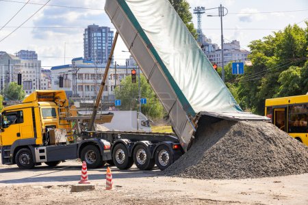 Car tonar for transportation of heavy bulk cargo large dump truck unloads cement sand mixture at road construction site.