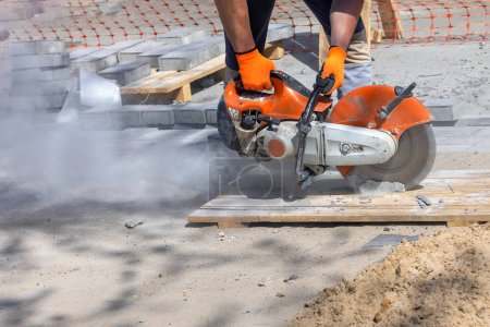 Photo for A worker cuts paving slabs with a petrol disc cutter, kicking up a cloud of dust behind him in the work area on a sunny summer day. Copy space. - Royalty Free Image