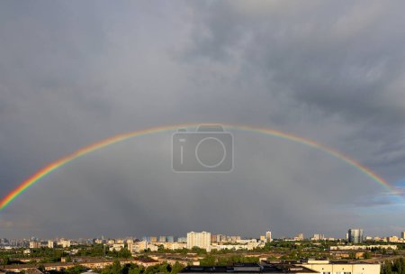 Photo for A colorful rainbow in the urban landscape over the roofs of city houses against a gray sky and in the sun. Copy space. - Royalty Free Image