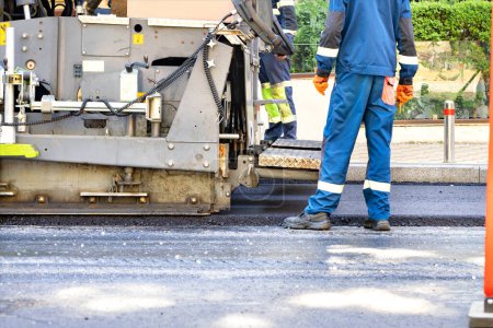 Photo for A fragment of the work of an asphalt paver under the control of workers at the construction of the road, the process of applying fresh asphalt is underway. Copy space. - Royalty Free Image