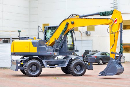 Photo for A wheeled construction excavator is parked in a paved car park on a bright day. Copy space. - Royalty Free Image