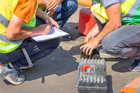 Foto de Los ingenieros de mantenimiento de carreteras miden el núcleo del pavimento de asfalto con una cinta métrica y registran los datos en una tabla. - Imagen libre de derechos