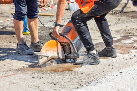 An einem sonnigen Sommertag schneidet ein Arbeiter mit einem Benzinkreiselfräser den Asphalt auf die Betonfahrbahn. Kopierraum.