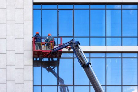 Workers wash glass windows of an office building in a crane bucket.
