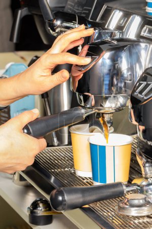 Foto de Las manos del camarero controlan la cafetera, el café espresso vierte el café en dos tazas de papel. Imagen vertical. - Imagen libre de derechos