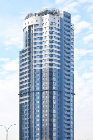 A slender residential skyscraper against the backdrop of a blue, slightly cloudy sky on a sunny day. Vertical image.