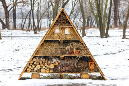 A winter hotel for insects among the snow made of straw, bamboo sticks, bricks, tiles, river pebbles, tree bark and tubular stems.