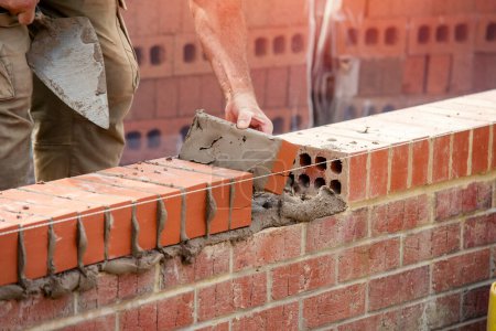 Téléchargez les photos : Industrial bricklayer laying bricks on cement mix on construction site close-up - en image libre de droit