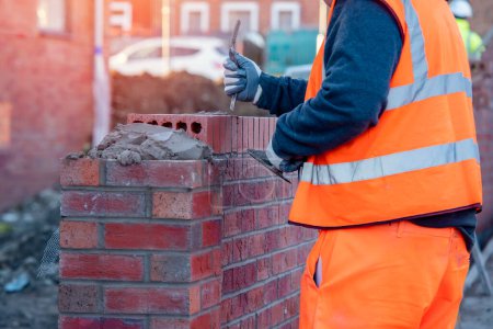 Téléchargez les photos : Industrial bricklayer laying bricks on cement mix on construction site - en image libre de droit