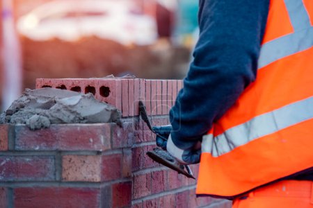 Téléchargez les photos : Close up of industrial bricklayer laying bricks on cement mix on construction site - en image libre de droit