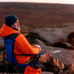 Bearded Man in orange jacket relaxing alone on the top of mountain and drinking hot coffee at sunrise. Travel Lifestyle concept The national park Peak District in England