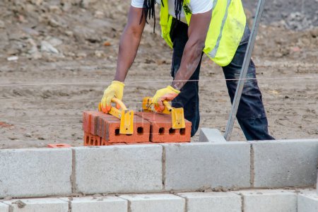 Téléchargez les photos : Hard working bricklayer lays bricks on cement mix on construction site. Fight housing crisis by building more affordable houses concept - en image libre de droit