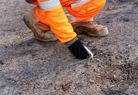 Téléchargez les photos : Surveyor opérant son instrument de commande à écran tactile pendant l'arpentage des travaux routiers et le point de marquage sur asphalte à l'aide de craie - en image libre de droit